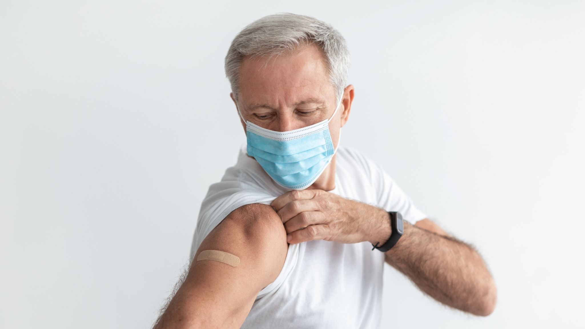 Older man in a face mask showing the bandage on his arm after a vaccination