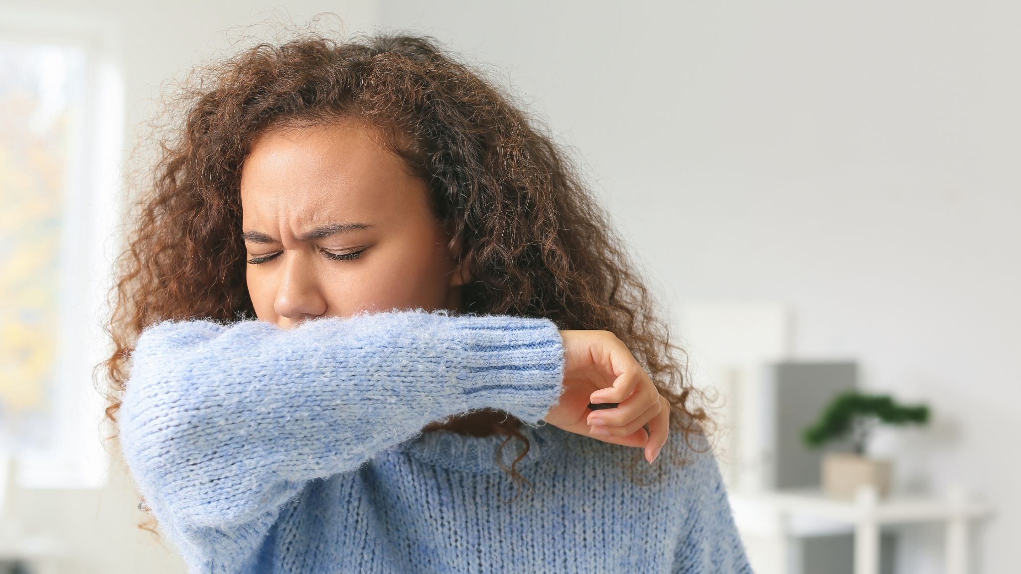 Young woman coughing into her elbow